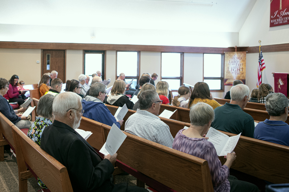members sitting in church reading pamphlets - Abiding Savior Evangelical Lutheran Church of Elk River, MN